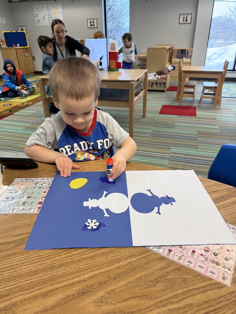 Head Start students sit at a table creating snowman shadow art, gluing paper pieces onto light and dark backgrounds.