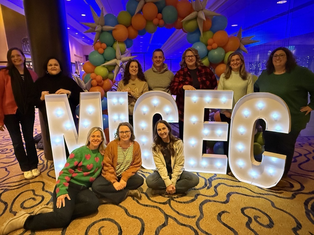 A group of people posing in front of a light-up sign that says "MICEC".