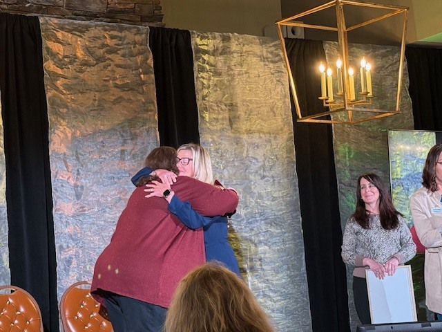 Two woman hugging on a stage.
