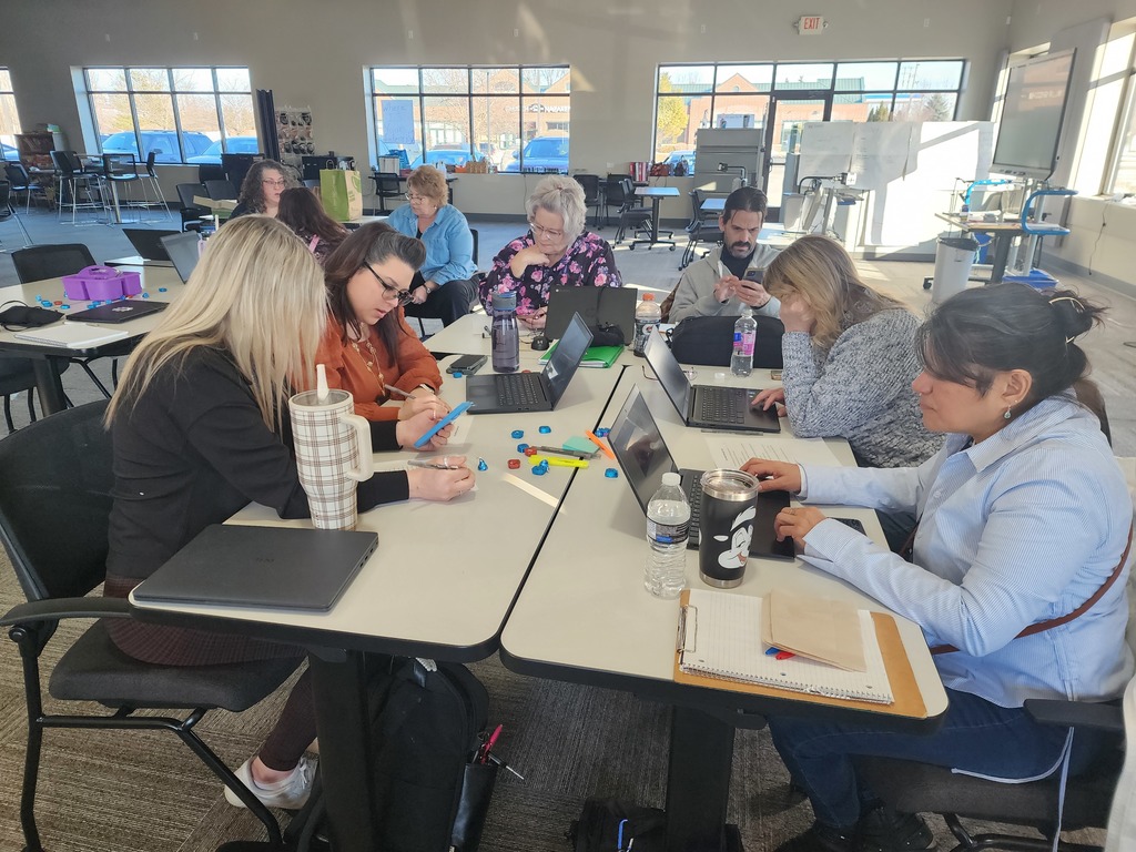 Adults sitting at classroom tables working on their laptops.