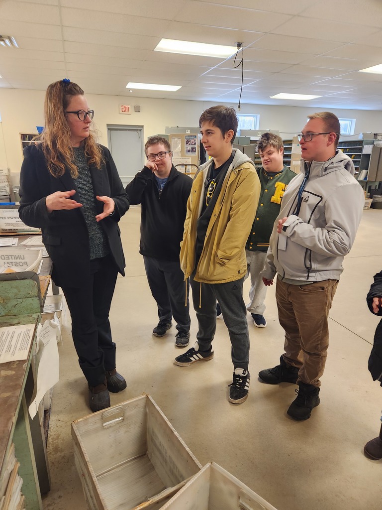 The Post Master is talking with young adult learners about jobs at the post office.