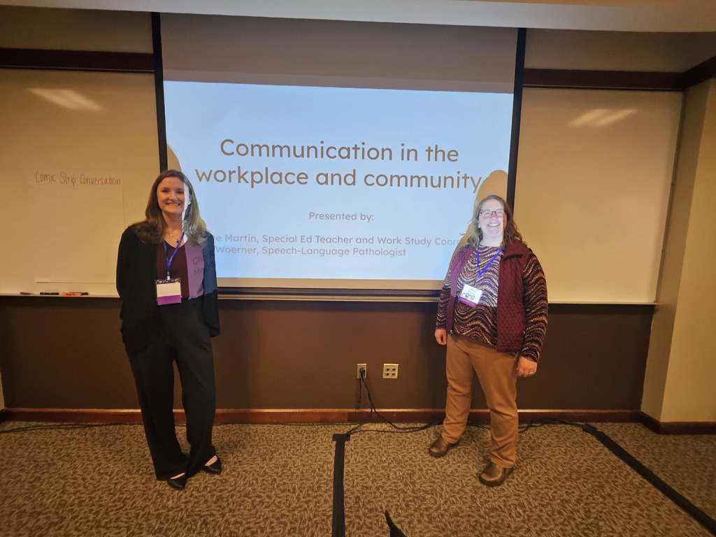 Two ladies standing near a screen that says Communication in the workplace and community