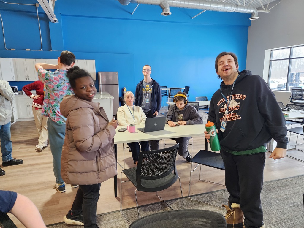Young adult learners standing around talking with a female administrator, in an educational setting. 
