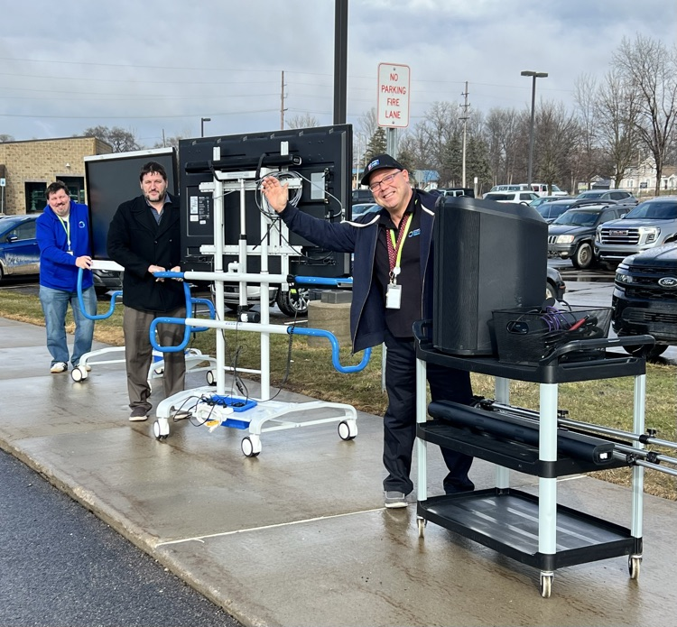Three men with very large TVs and speakers walking 