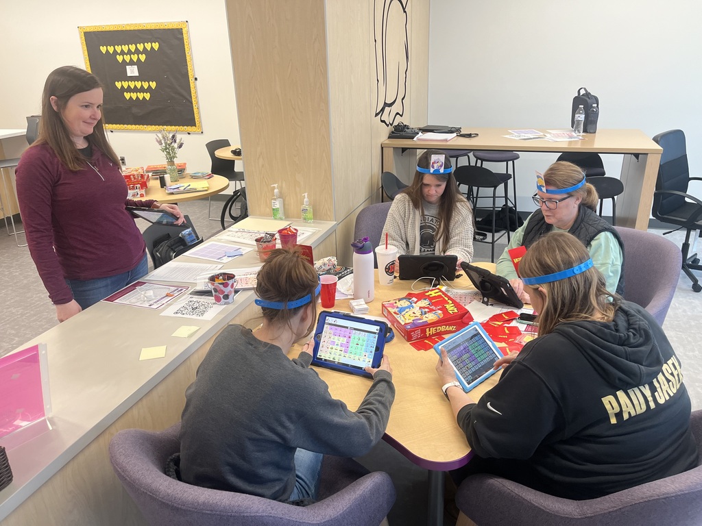 4 adults around a table playing Hedbanz game and using AAC devices.