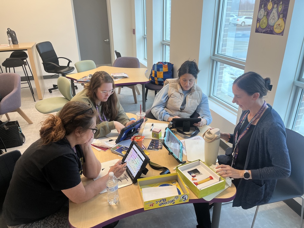 4 adult women around a table playing a game and using AAC devices.