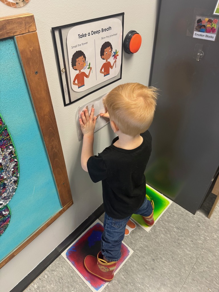 Preschool children standing in the classroom Big Breath area, pressing their hands to the wall beneath a “Take a Deep Breath” poster while standing on sensory floor spots.