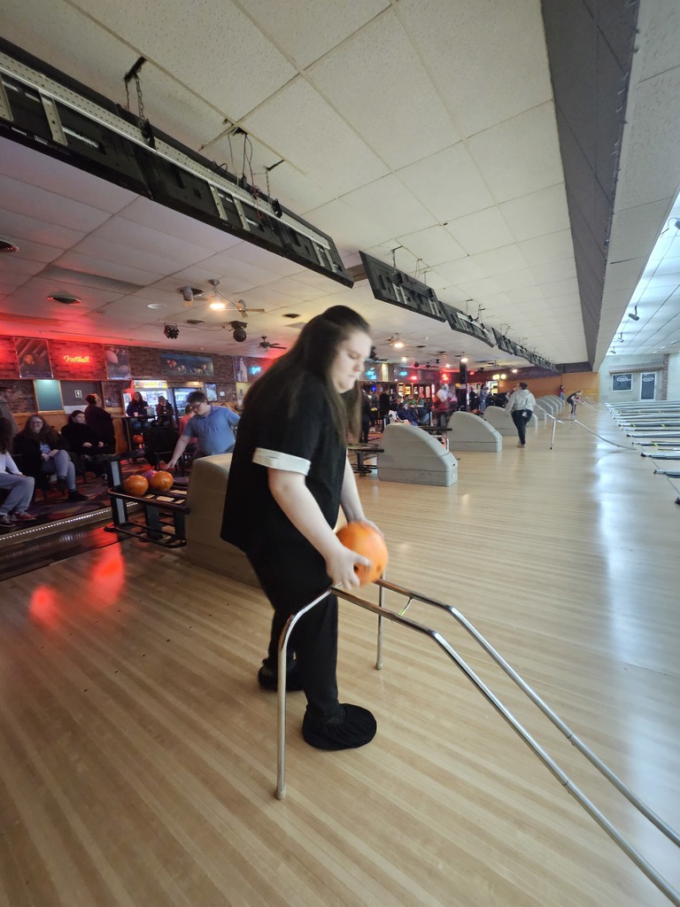 A woman in a black short-sleeved shirt with white stripes on the sleeves carefully positions a ball on a ramp
