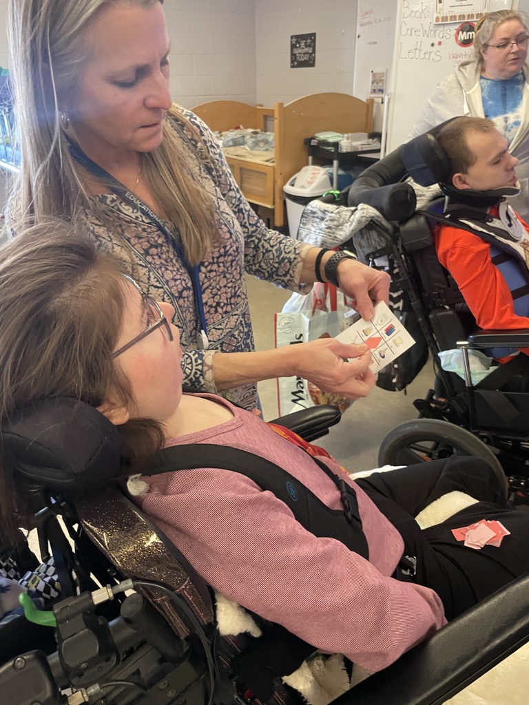 Young adult in a wheelchair working with an assistant who's holding up a bingo card.