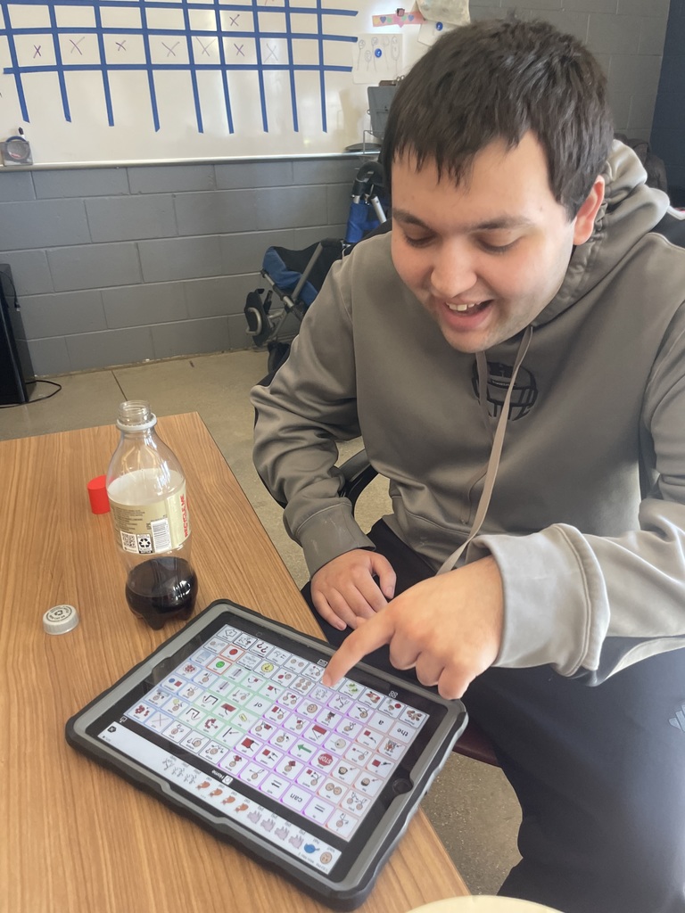 Student sitting at a table, pushing an icon on his AAC device.