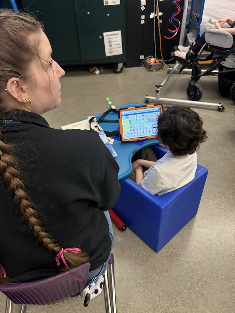 A student sitting down with their AAC device