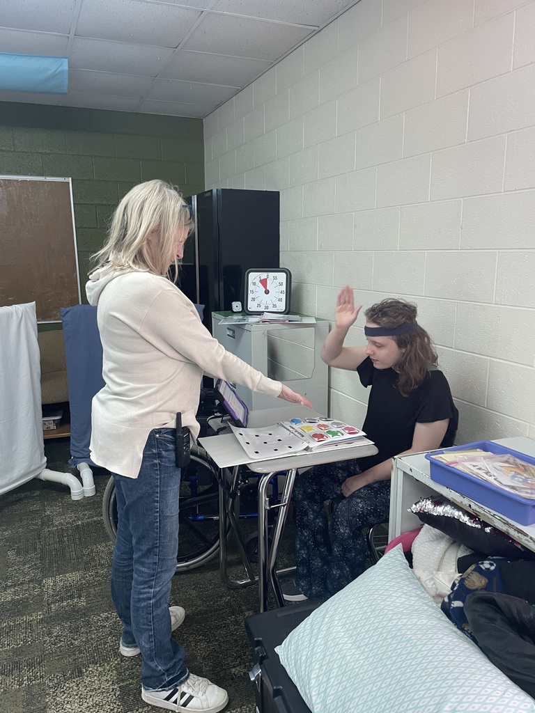 Student siting at a desk, with work in her table, giving an adult an high five. 