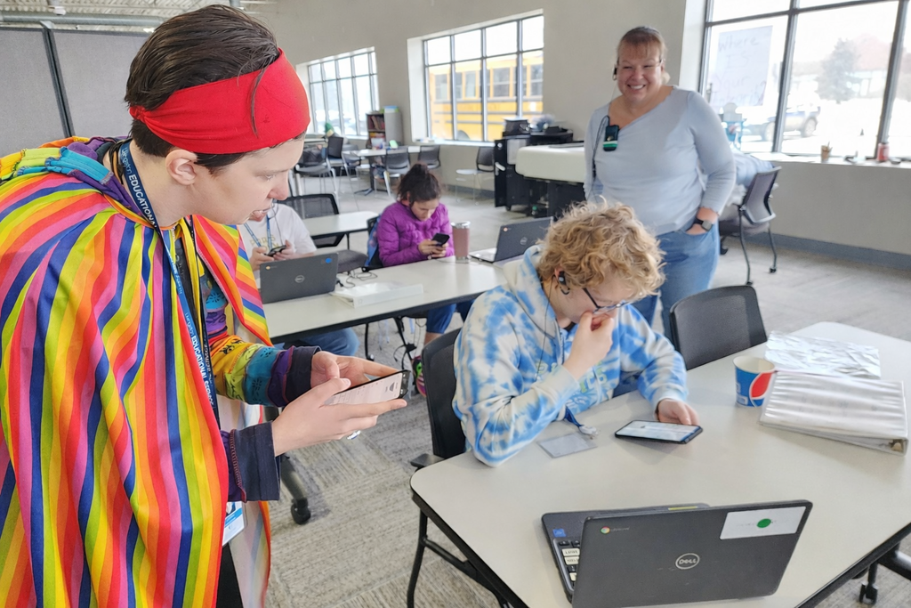 Two young adult learners with phones in hand and a teacher looking on.
