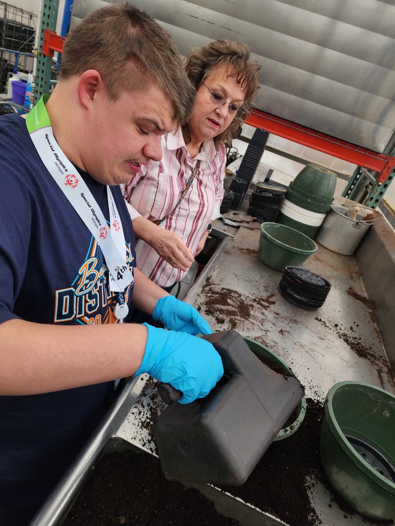 Teacaher and young adult filling floer pots with soil.