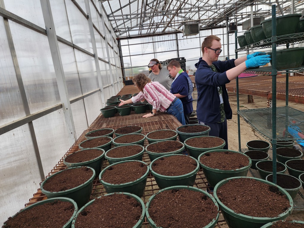 Adults moving flower pots to growing tables.