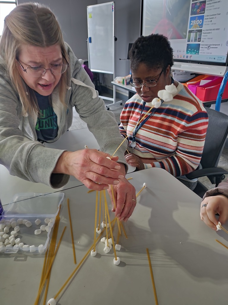 A teacher and a young adult learner building with spaghetti noodles and marshmellos.