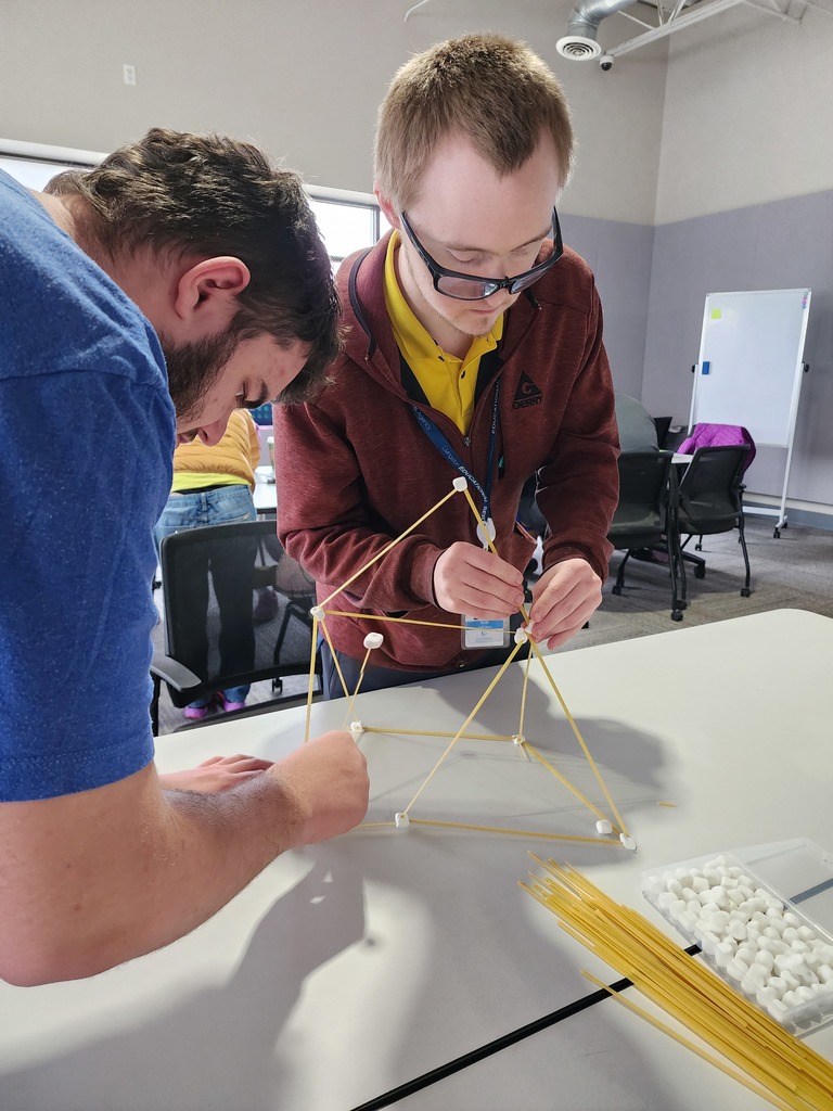 Two young adults building with spaghetti and marshmellos.