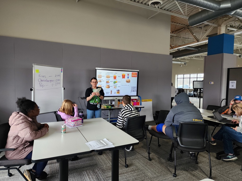  A teacher standinjg in front of a class of young adult students.