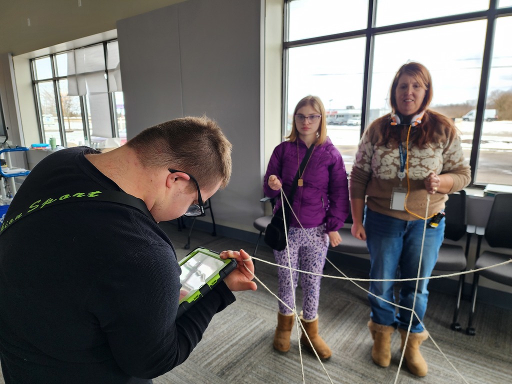  A teacher,  young adult female  and a yound adult male holding a communication device with strings hanging on their fingers.