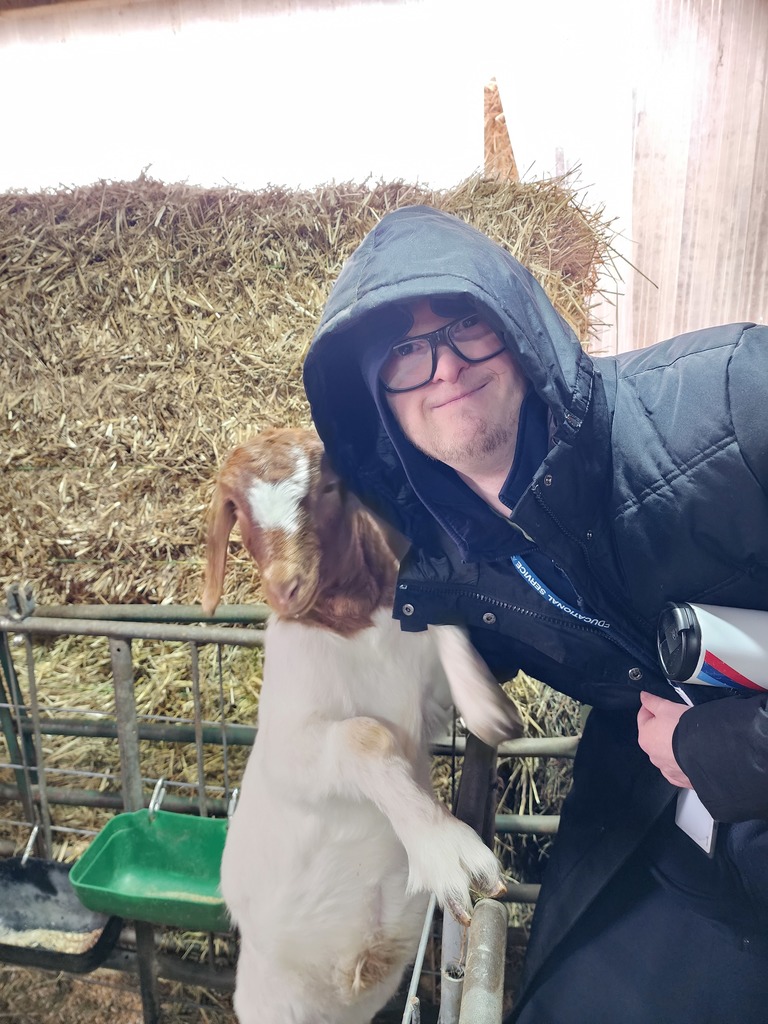 A young adult male standing with a goat.