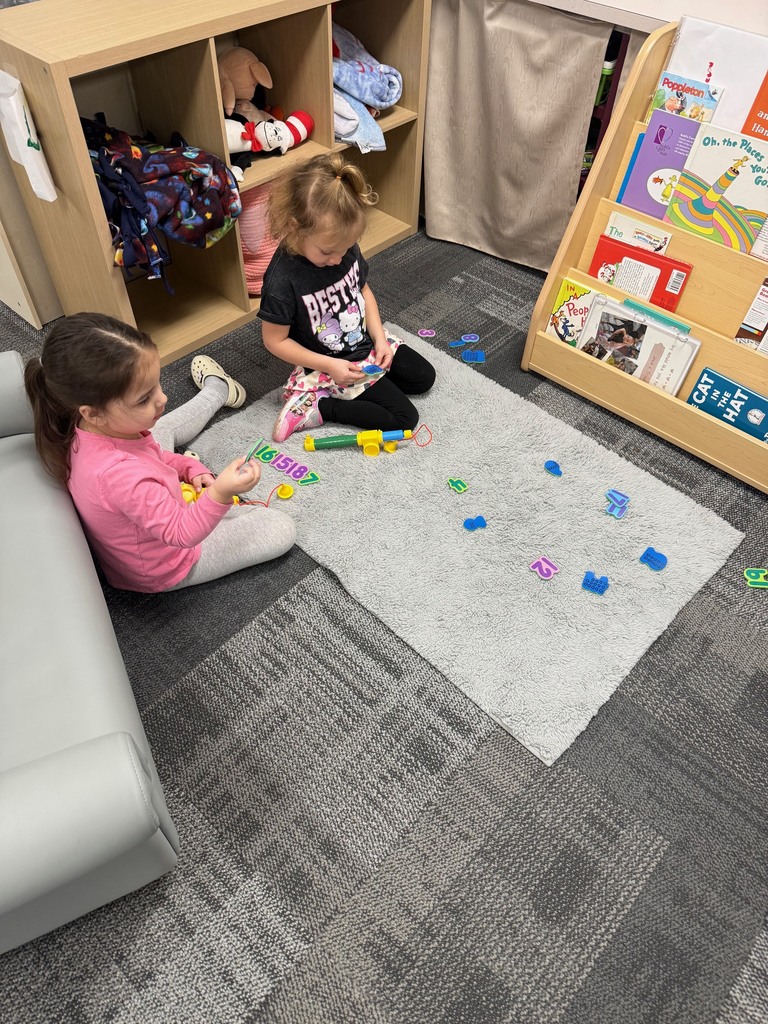 Preschool children sit on a rug using toy fishing rods to catch number pieces and count the raised dots on the back.