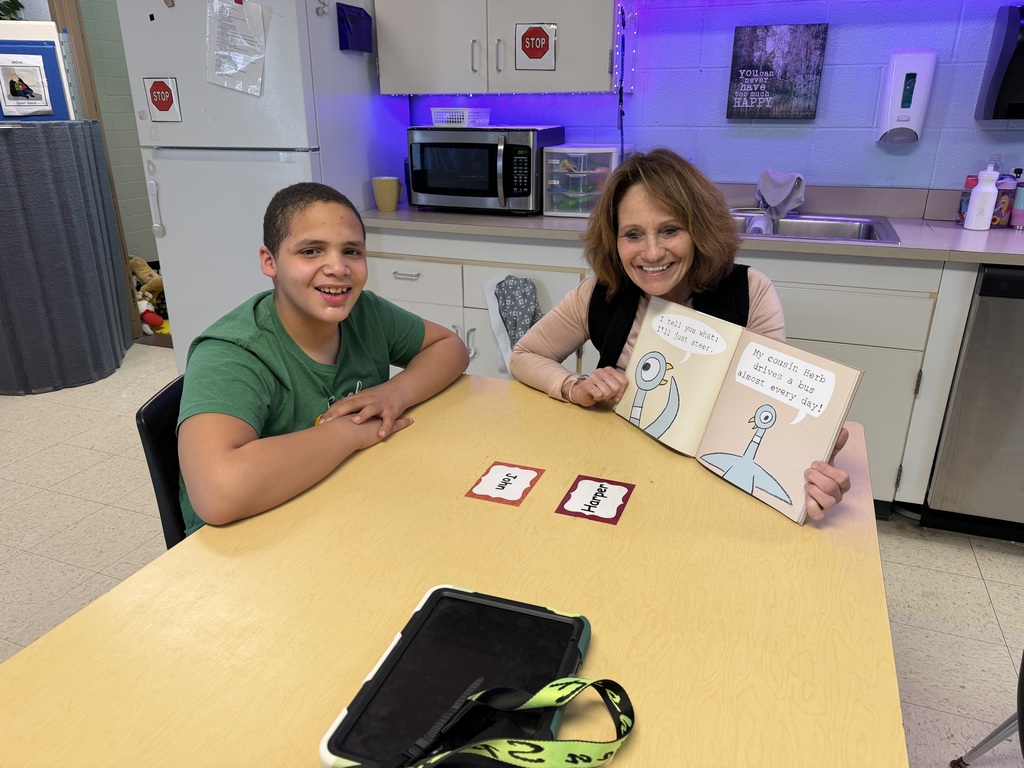 Student and staff sitting at a table reading a book.