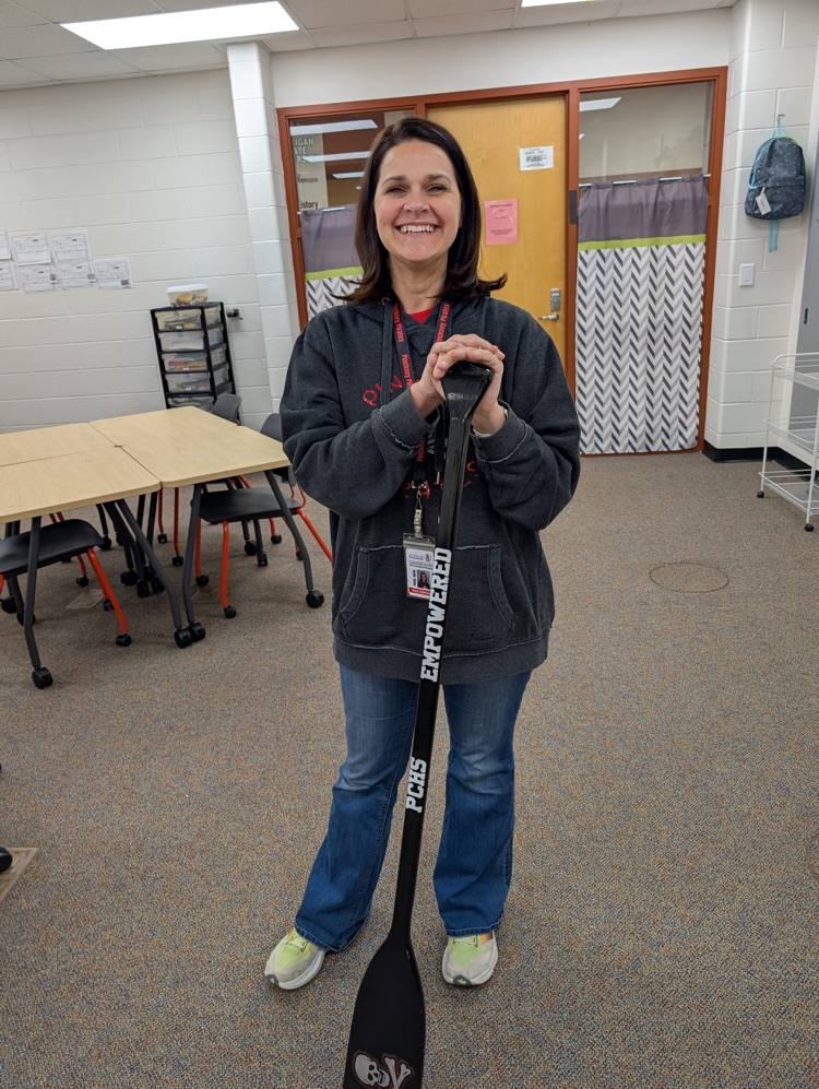 Woman grinning while posing with a Pinckney High School themed rowing ore. The words "Empowered" are stamped across the handle.