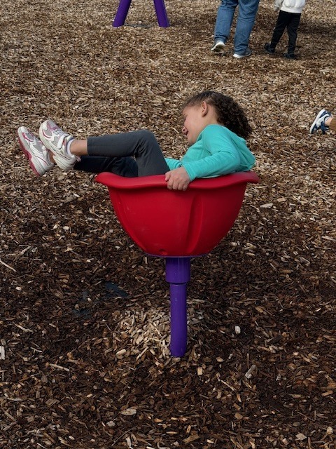 Child lying sideways in a red spinning playground bowl on wood chips.