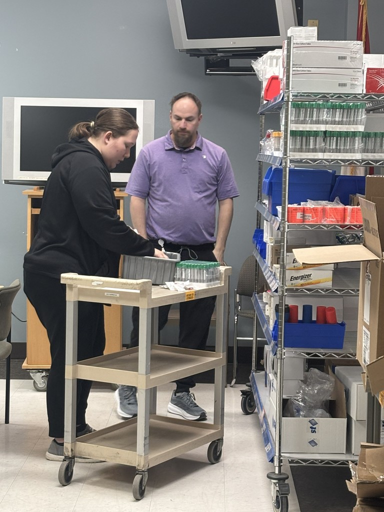 Two people organizing medical supplies on a utility cart in a storage room.
