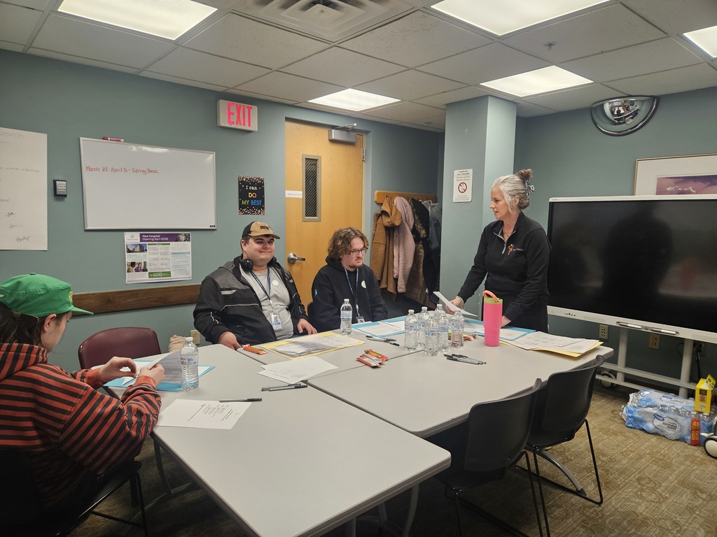 A woman leading a meeting or training session for three young men seated at a table.