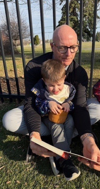 A young kid sitting on the lap of an man with glasses, reading a book.