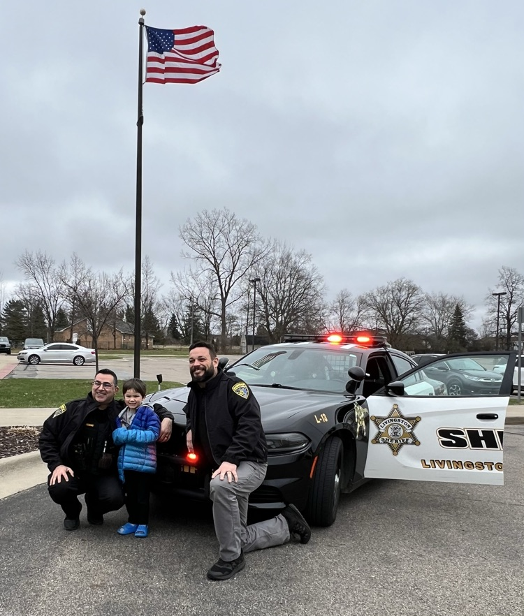 Two deputies and young boy posing for a photo in front of a patrol car 