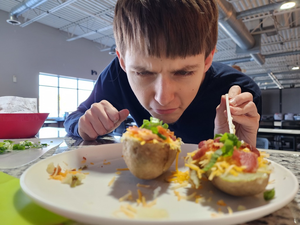 Young adult looking at a loaded baked potatoes that he made.
