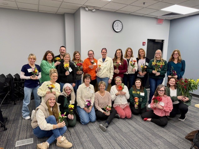 Group of instructional coaches standing together, holding vases with bouquets and smiling for a group photo.