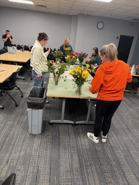 Adults gathered around a table, selecting flowers from shared vases.
