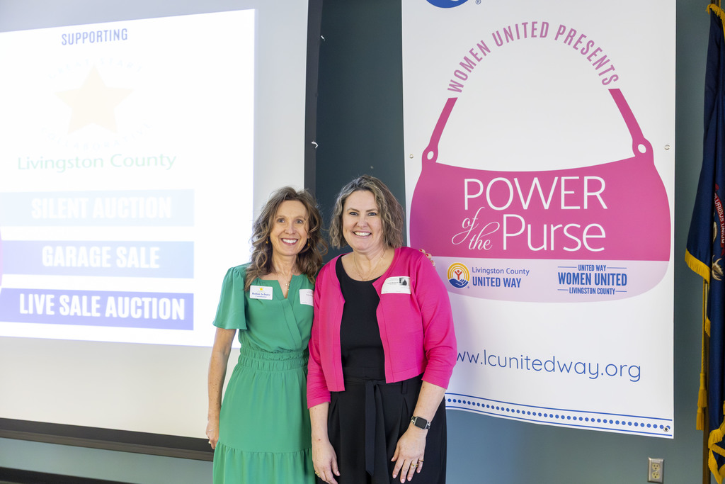 Two women standing together in front of sign. 