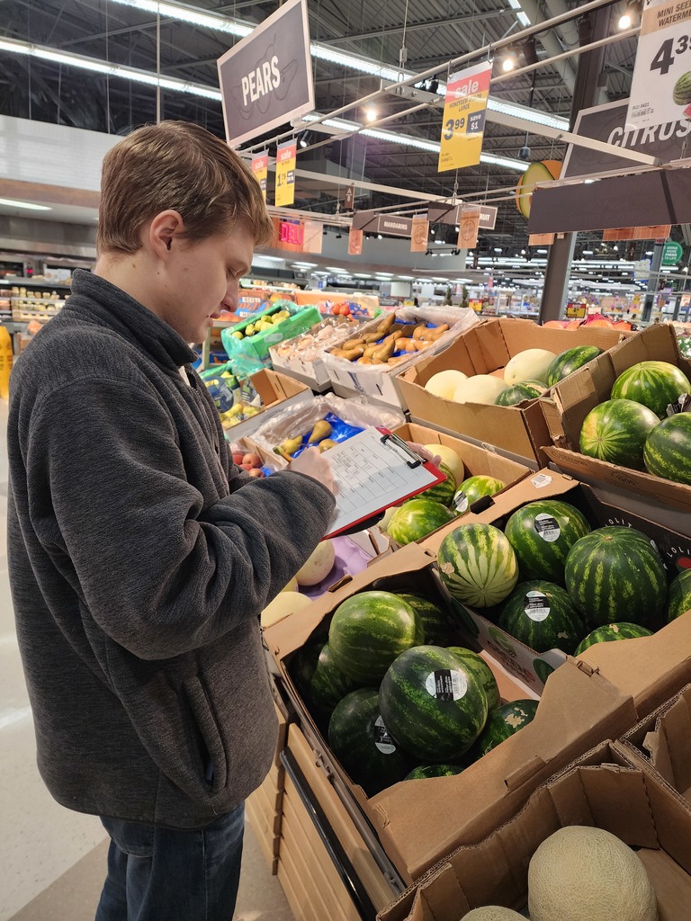 A young adult male looking at prices of fruit.