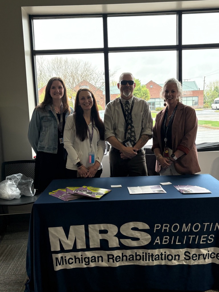 Four smiling people standing behind a table with a Michigan Rehabilitation Services banner.