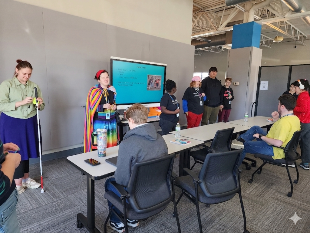 Young adult male and females standing in front of a room talking to a classroom of learners.