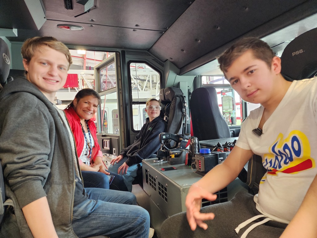 A female teacher and three male learners sitting in a fire truck.