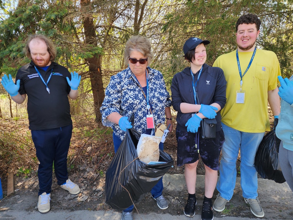 Young adult learners and a staff member holding a bag of trash for Earth Day clean up.