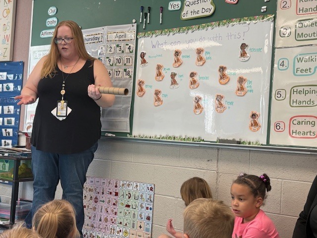 A preschool teacher leads a “Question of the Day” activity, guiding children as they discuss and share ideas for how to use a paper towel roll.