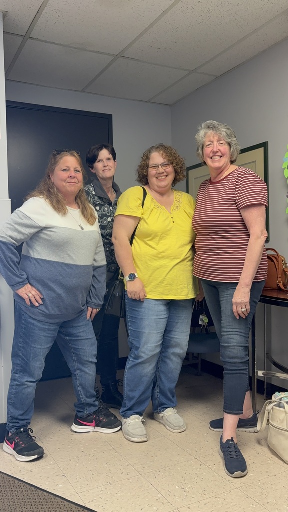 Four smiling woman standing together and posing for a group photo in an office setting.