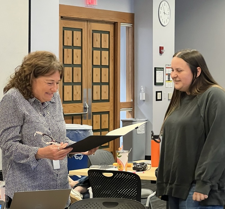A woman smiling while reading through a certificate she had just received from another woman.