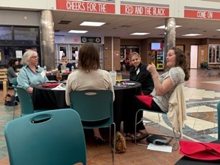 Four women sit a round table chatting.