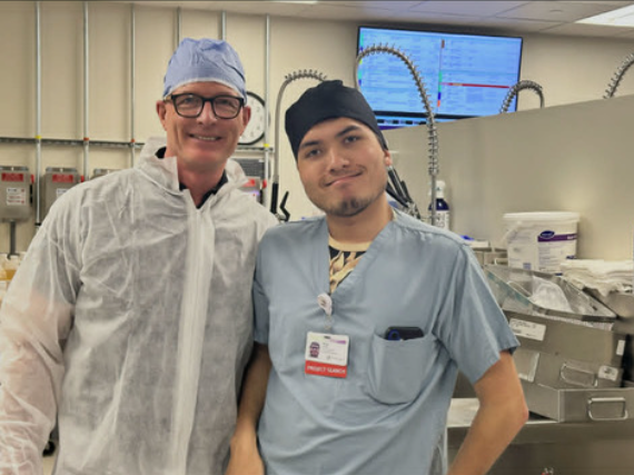 Two men in medical scrubs and protective gear smiling for a photo in a clinical workshop.