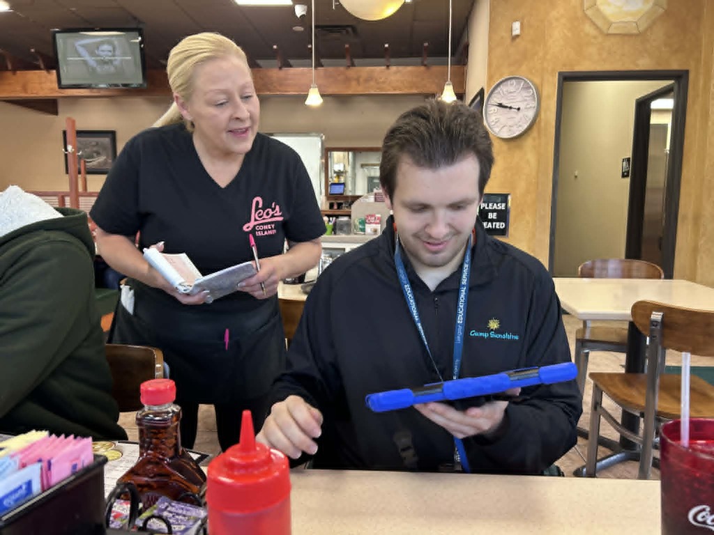 Student using an AAC device to independently order at Leo’s Coney Island.