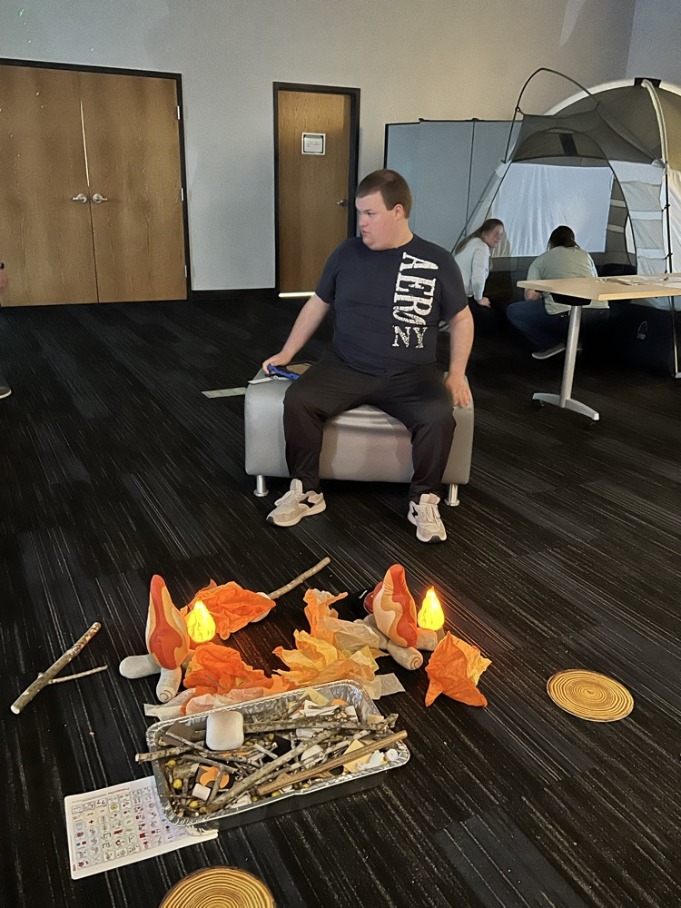 Young man sits by a makeshift camp fire.