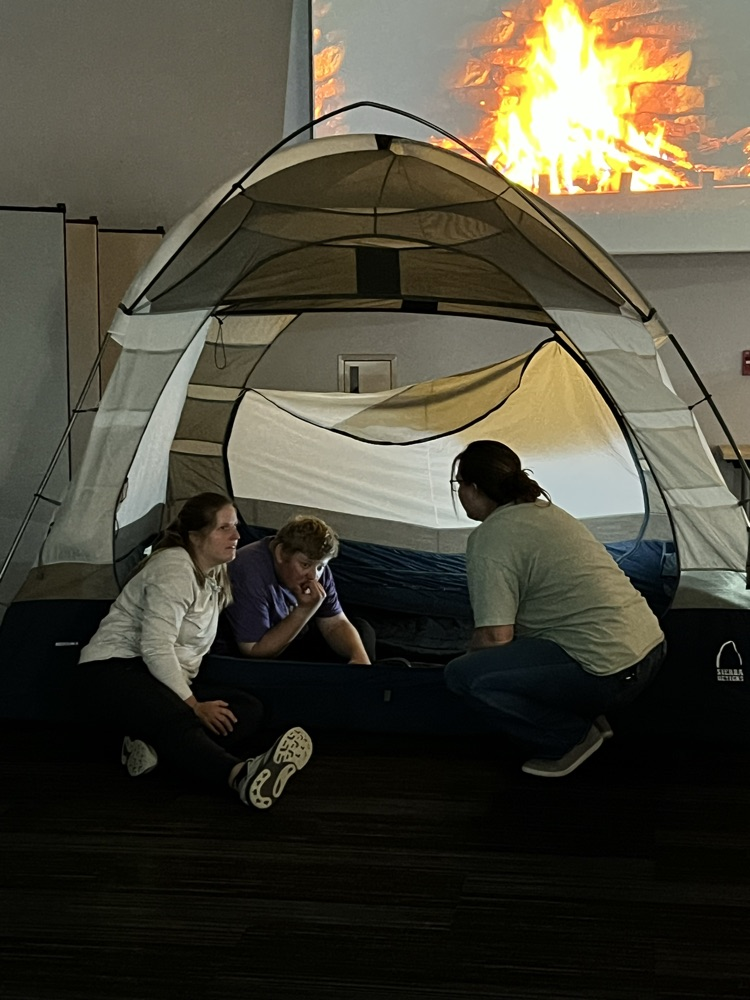 Two teachers sit with a learner inside a pop up tent.