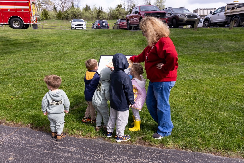 Adult women standing with group of small children looking at a plaque.